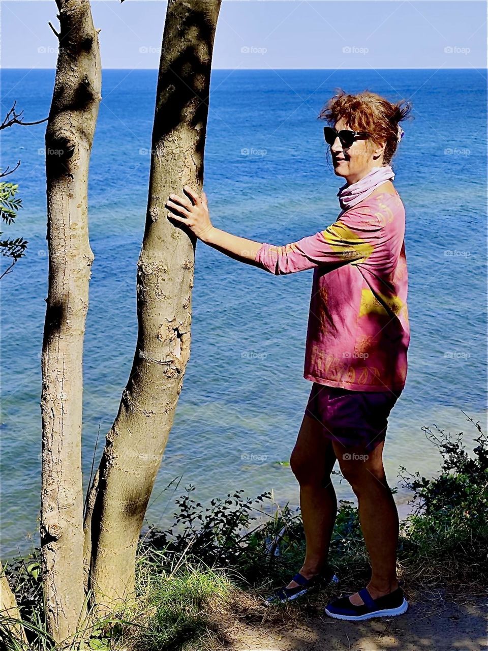 Holding onto a tree trunk on the beach of the “Baltic Sea”, the “Ostsee” as locals call it on the island “Rügen” in “Mecklenburg - Western Pomerania”, Germany our lady is taking in the sights on a beautiful day in August 2024. Hypnotic Productions