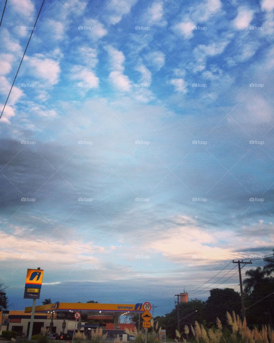 Amanhecer de céu azul com nuvens que decoram a paisagem. Abaixo, no canto, o Posto Harmonia (que é IPIRANGA). 