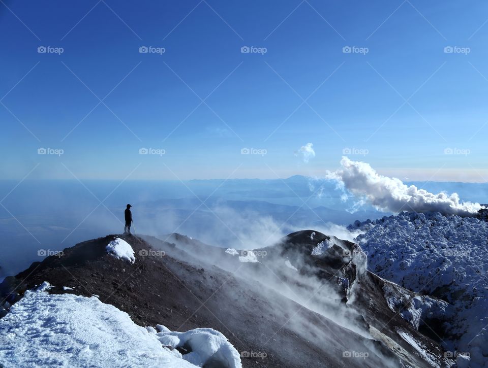 silhouette of a man who stands on a volcano and looks at the blue sky