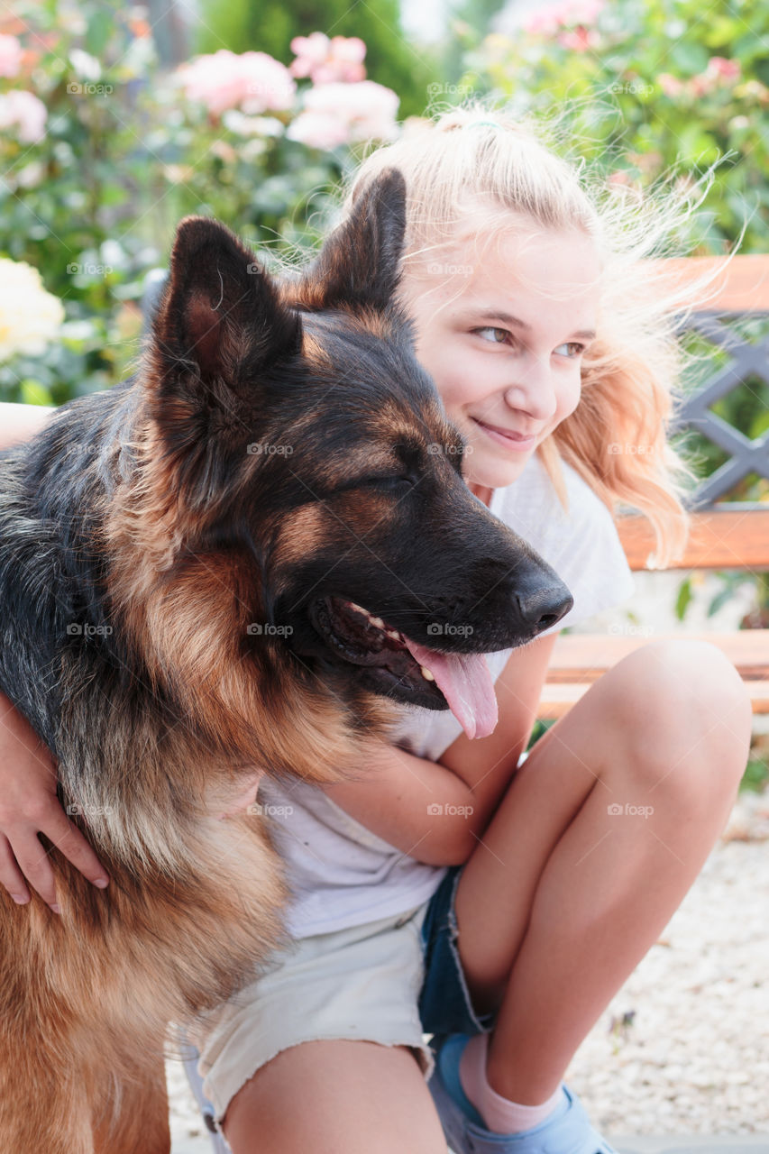 Young smiling girl squatting in the garden and hugging her dog