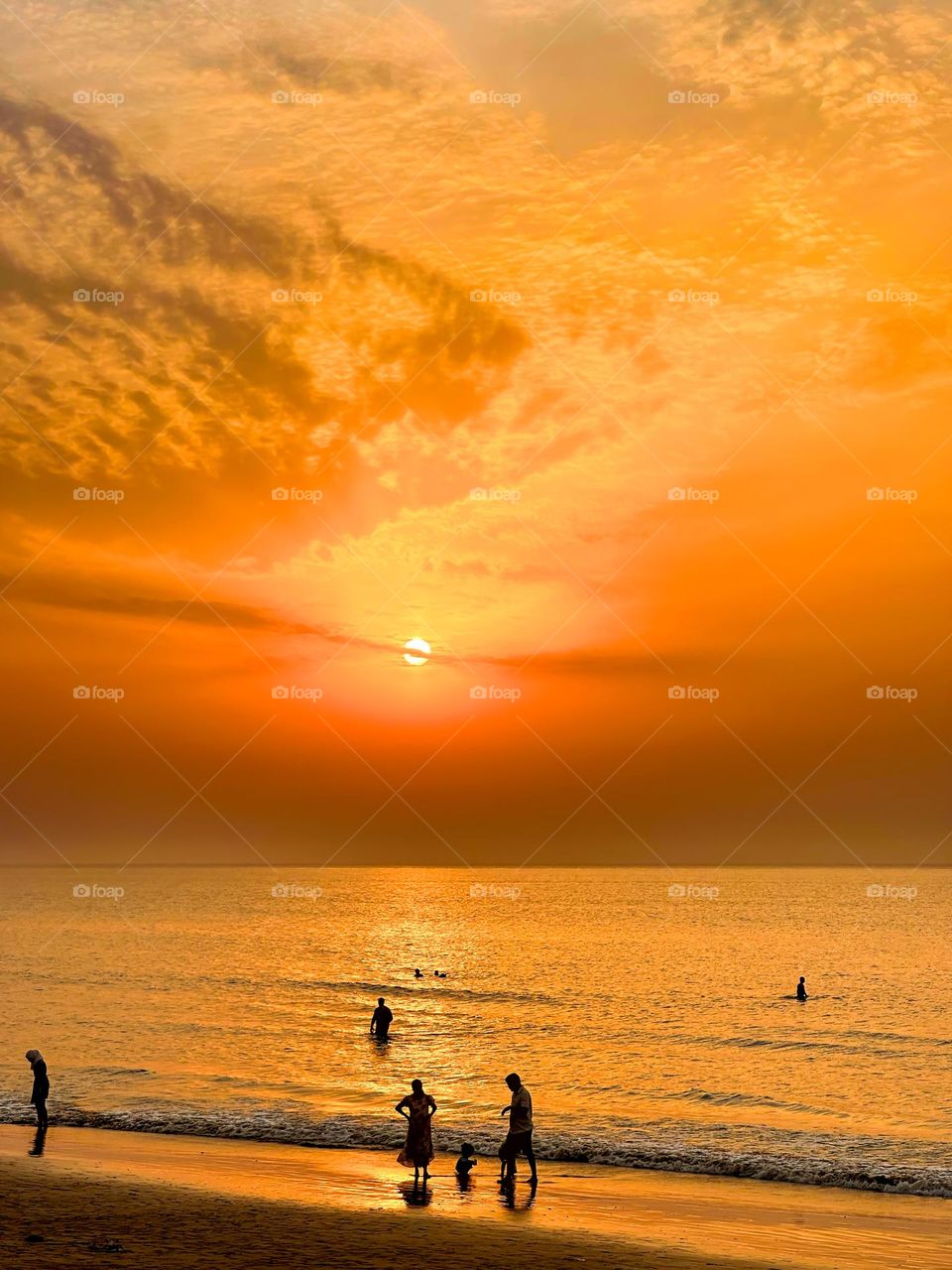 Golden sunset over the beach with silhouettes of people enjoying the tranquil waters.