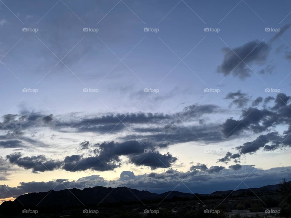 A sunset with mountains and multiple dark storm clouds. 