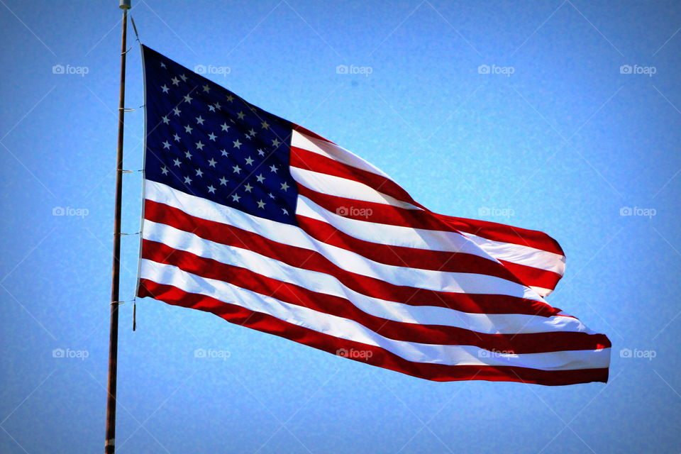This is a picture of the American flag flying high in the bright blue sky on a beautiful spring day.