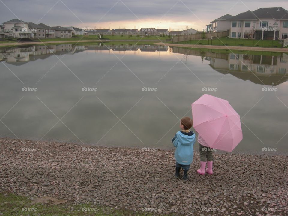 Kids looking across the lake with a pink umbrella 