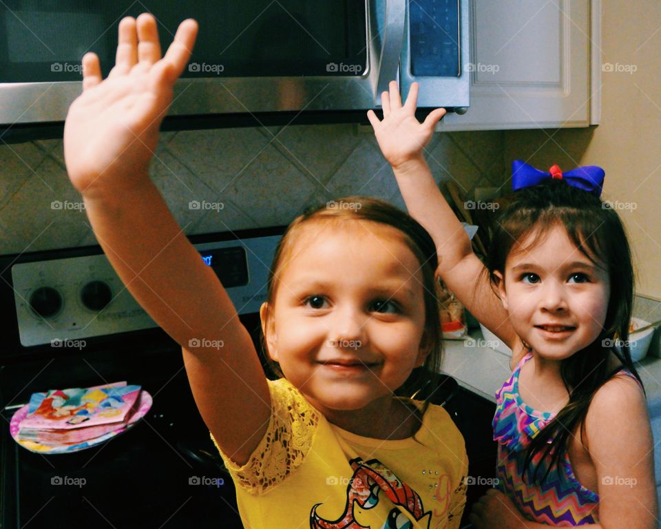 Little sisters standing in kitchen raising their arm