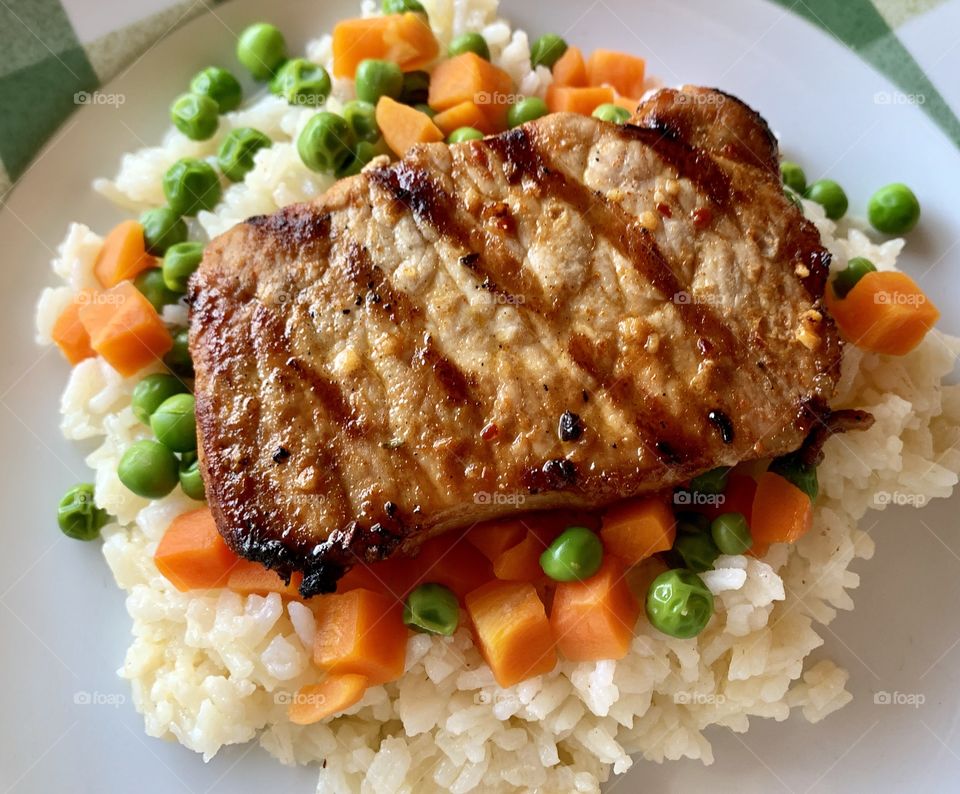 Delicious chili powder and garlic rice covered in colorful veggies of peas and carrots.  Topped with beautifully grilled spicy pork chops.