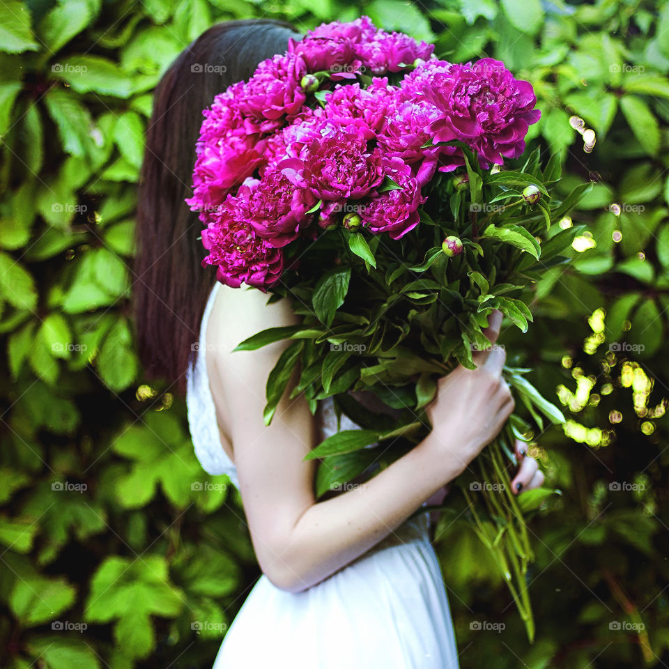 Beautiful portrait of redhead girl in white dress with a spring huge bouquet of fresh pink peonies on her hands.