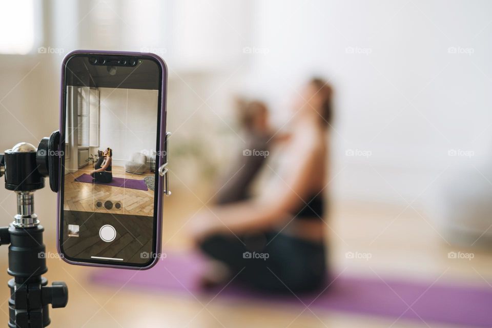 Young woman with little daughter fitness blogger doing exercises and recording video on mobile phone in studio