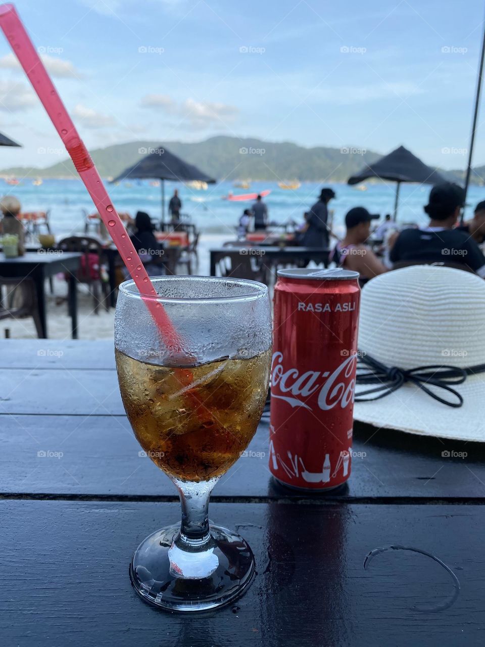 A glass and a can of coca cola on a table with a sea view.