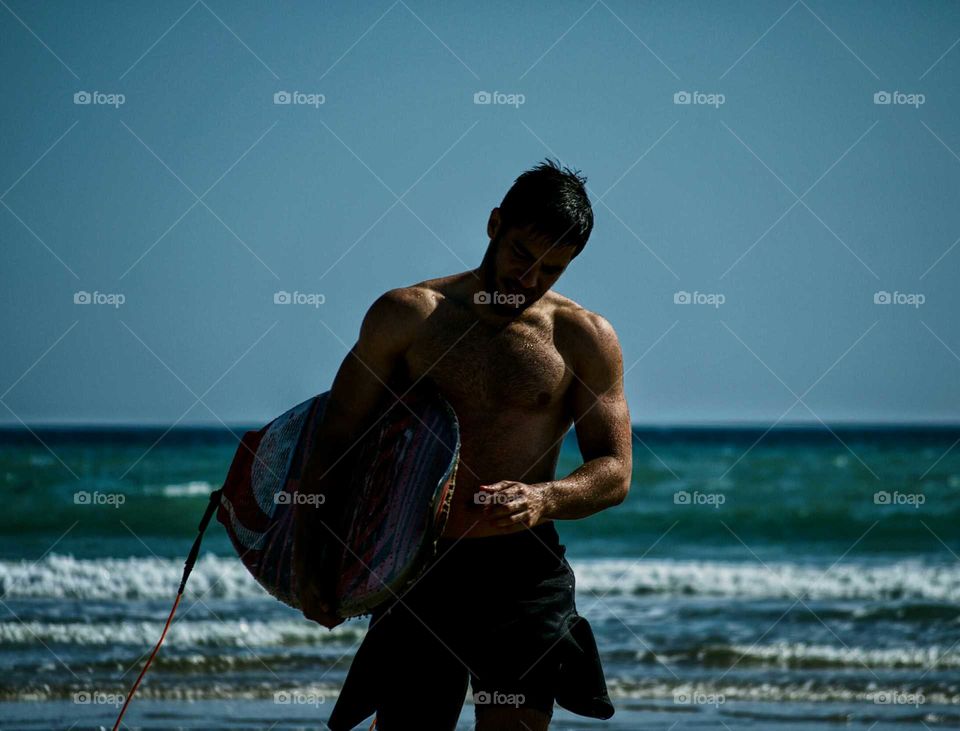 Shirtless man holding body board standing in front of sea