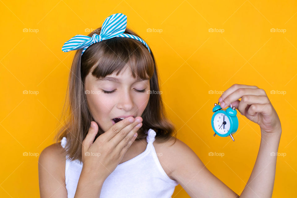 Teenager girl yawns and holding alarm clock