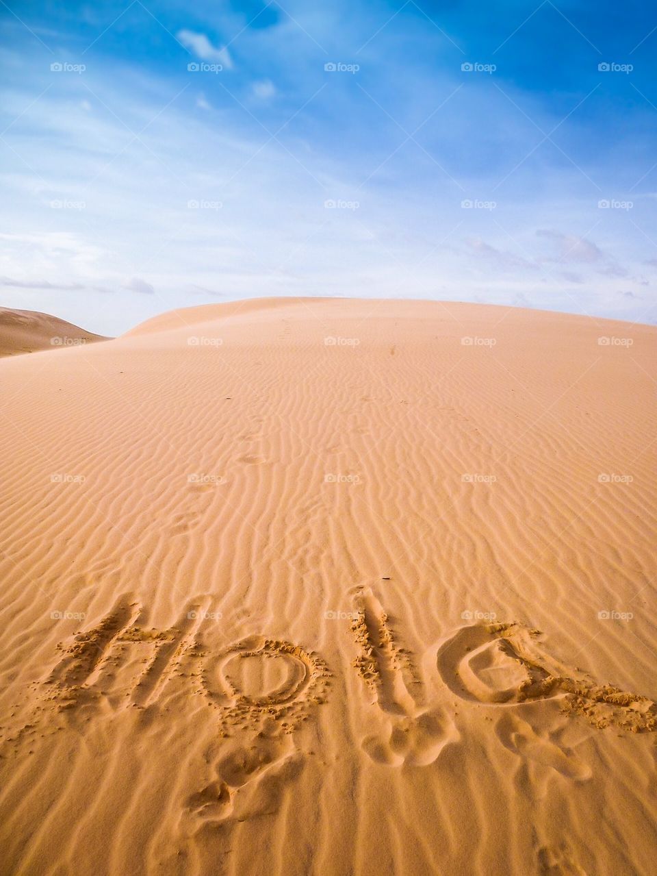 Greetings in Spanish written on sand. Hola.