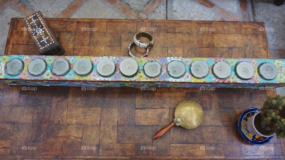 A table top made out of a wooden door with a tea candle holder, crumb gather, a green plant, bracelets and an inlaid wooden box.