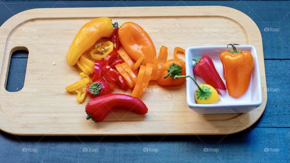 A small cutting board with three cut up sweet peppers on it and a creamy dip to the side
