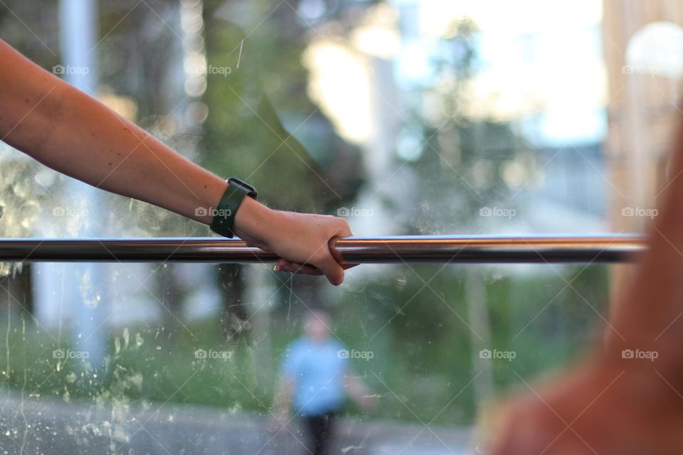 Arm of a woman holding onto a pole at the dirty window of a tram