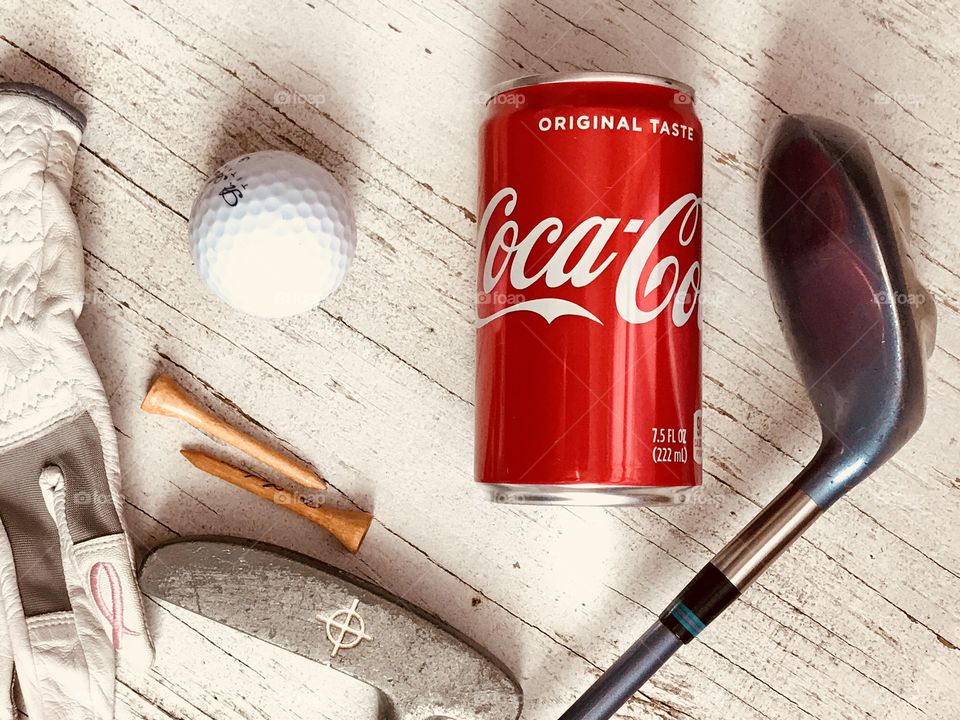 A can of Coca Cola with golf equipment on a rustic white background 