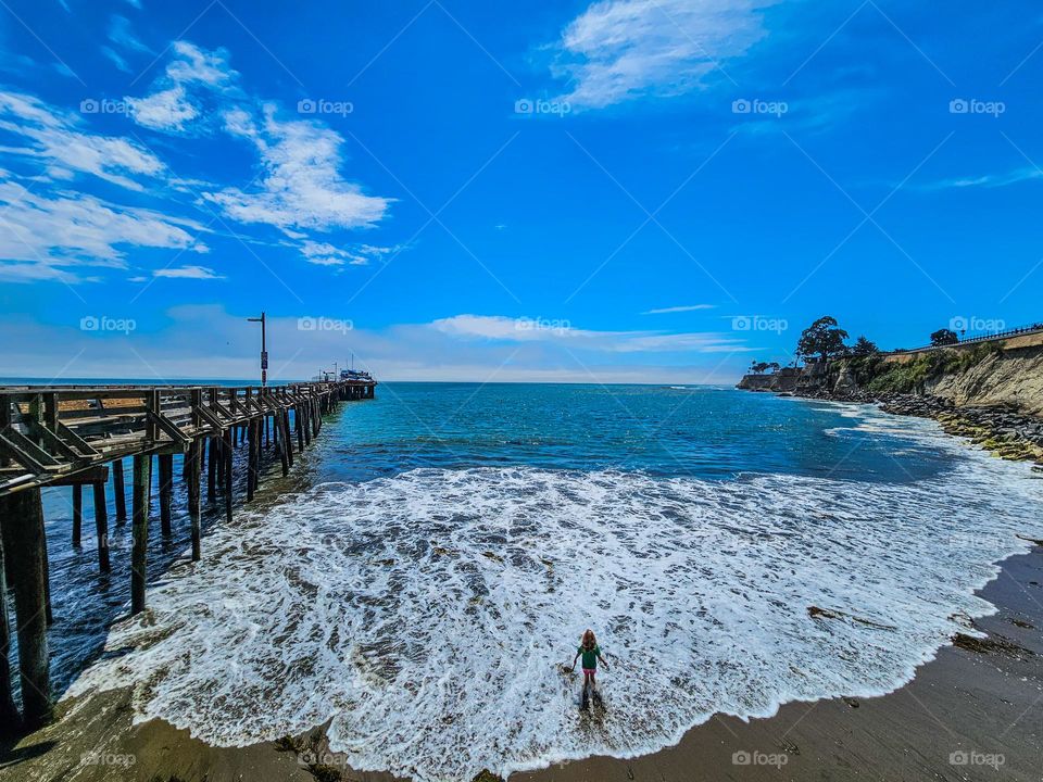 Little girl wading in the ocean water as a wave cascades onto the beach in Capitola California on a beautiful summer day 