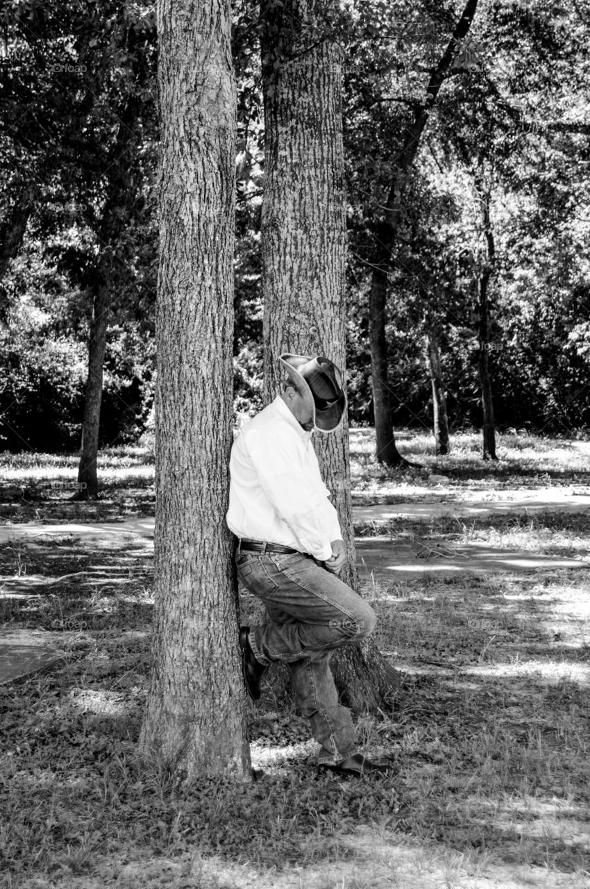 Cowboy leaning against tree in black and white