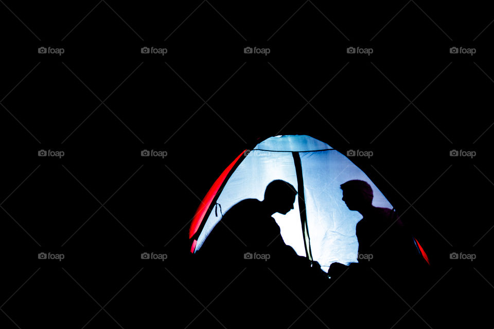 Picture of two guys with a flashlight on inside a tent.