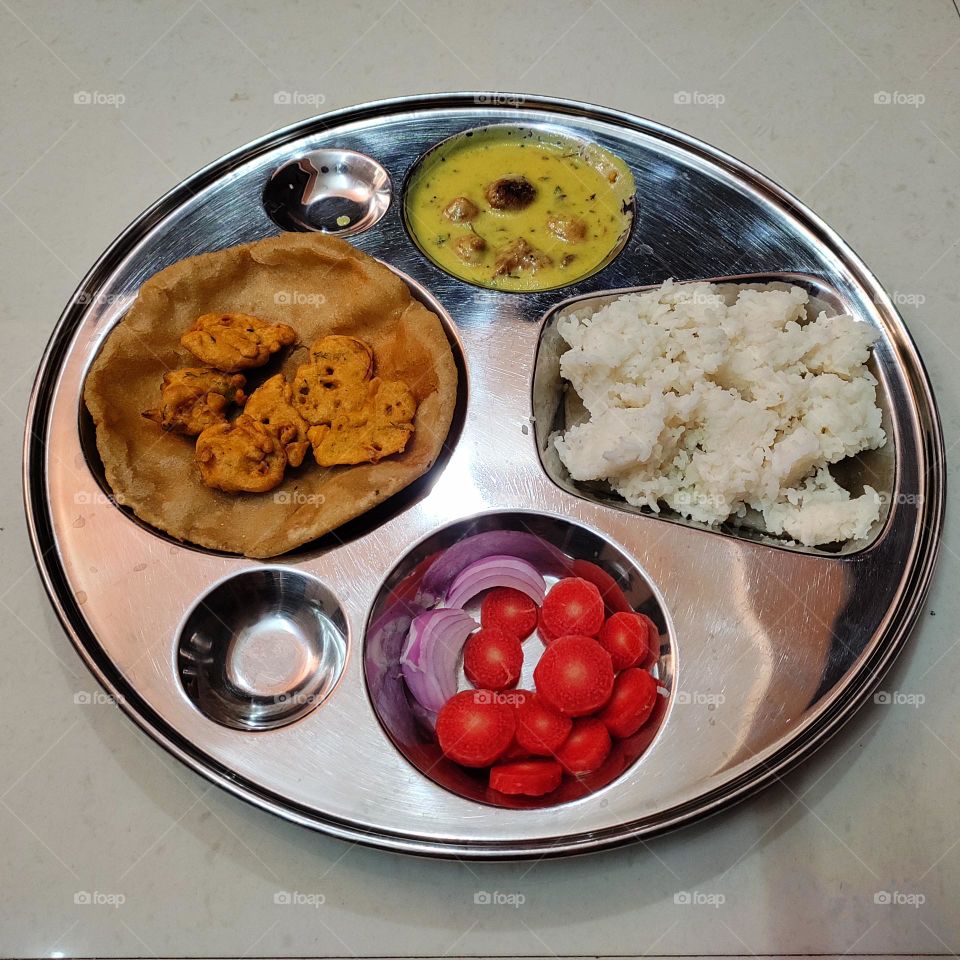 India food: curry pakoda, fritters, rice, puri, and a healthy corner of salad with carrot and onion.