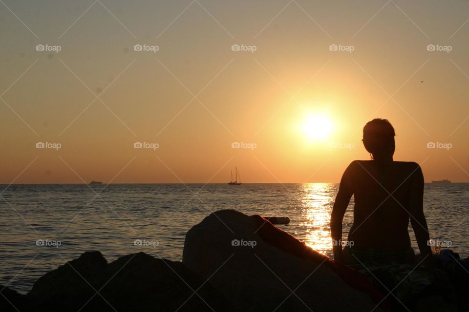 Silhouette of a Woman sitting on the rock watching sunset at the sea