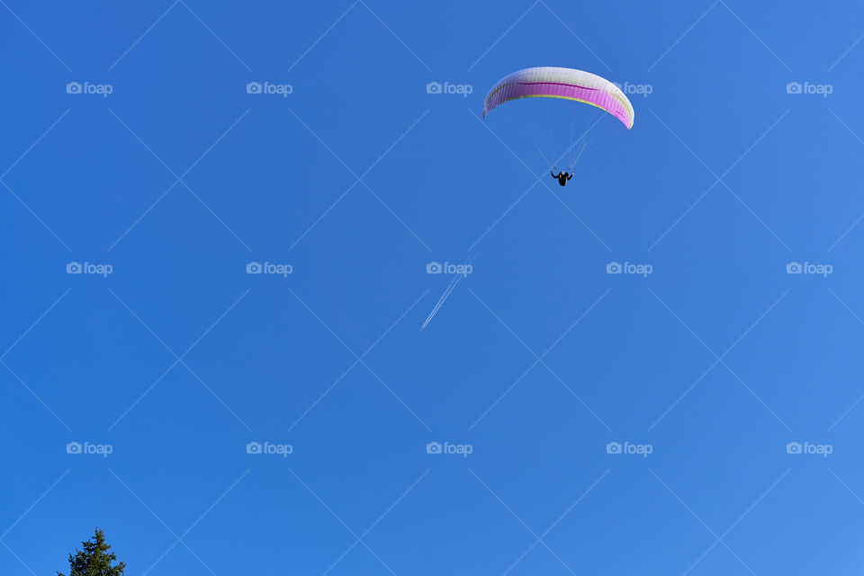 Paraglider and an airplane leaving behind a white trail in the sky 