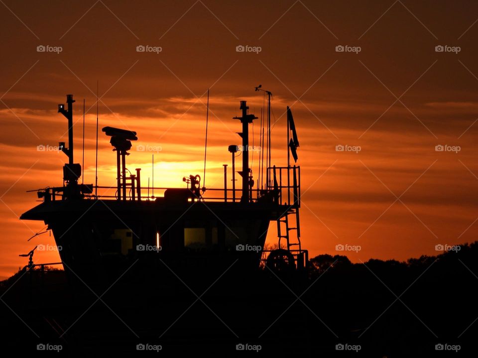 A tugboat cabin silhouette sitting at the dock at sunset with a light and an array of antennas 