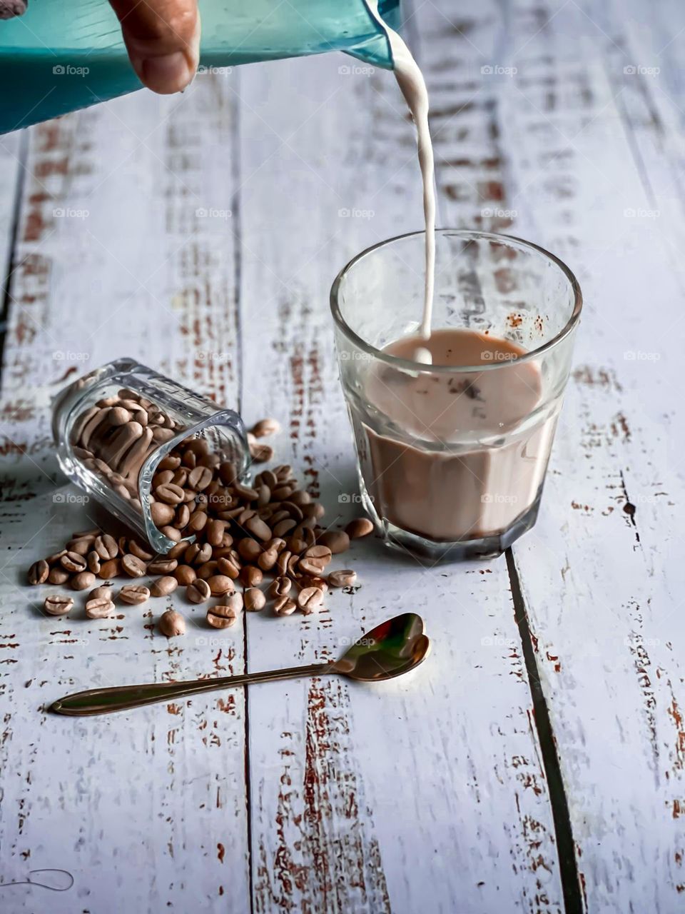 Pouring milk into a cup of coffee with spilled coffee beans on the side in close up view