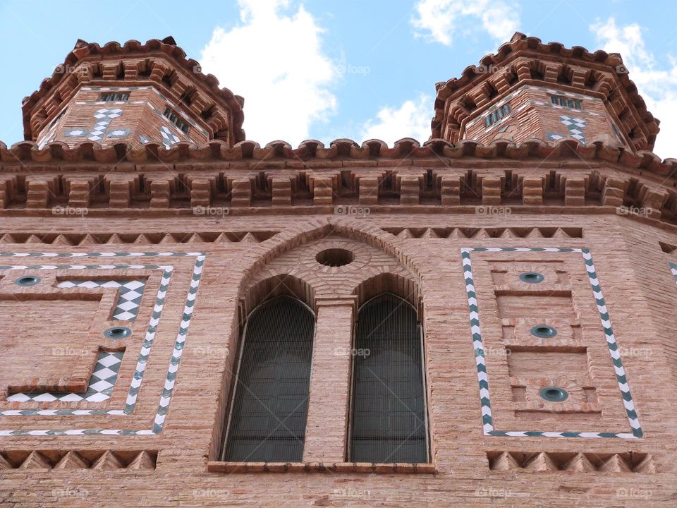 Spanish gothic church with red stones and blue decorations, blue sky and white clouds.