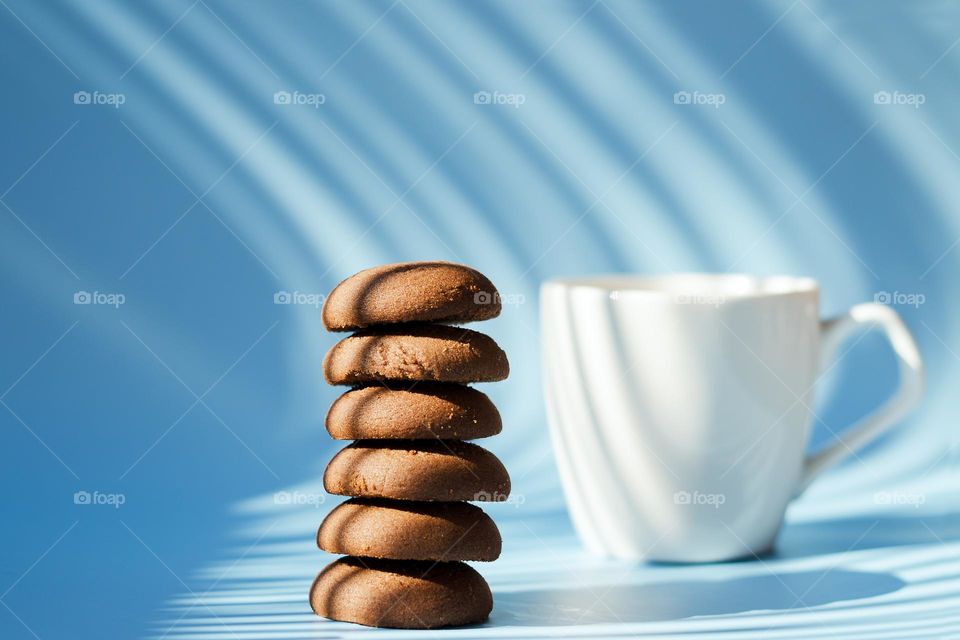 top view of sweet delicious chocolate cookies and cup of hot black coffee,  tea. Blue background.