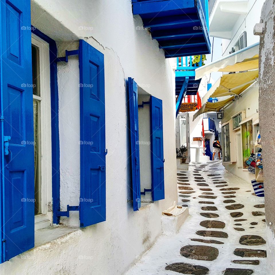Typical lane in Mykonos, with white-washed walls, bright blue shutters & white-edged paving
