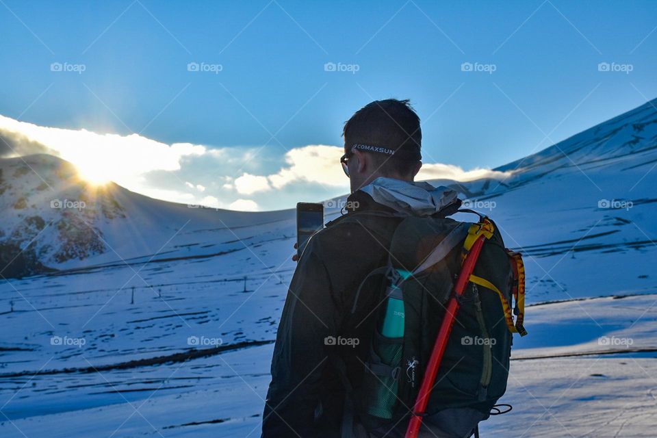 Man taking a picture Of the sunset in the snow 