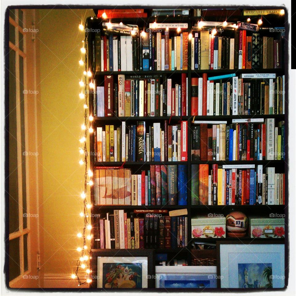bookshelf lit up. a full bookshelf with Christmas lights, bathed in a warm glow