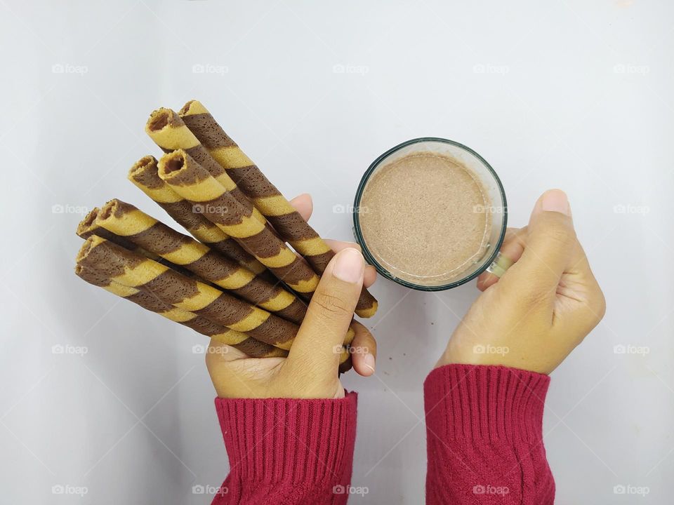 Holding some wafer roll sticks and a glass of chocolate milk on white background. Top view