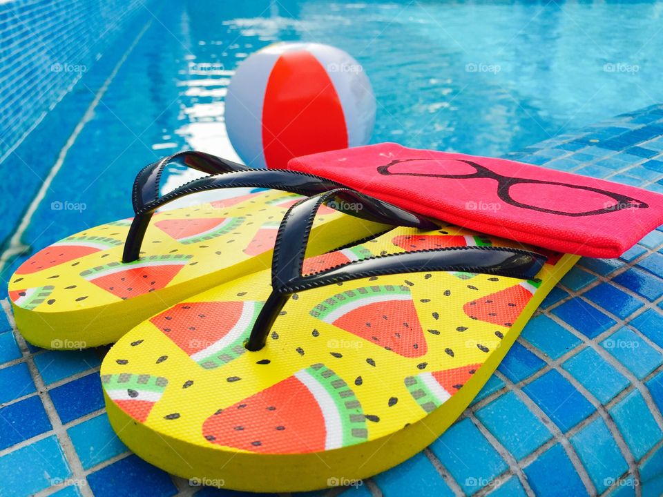 Flip flops with watermelons,pink sunglasses case and water ball near the pool