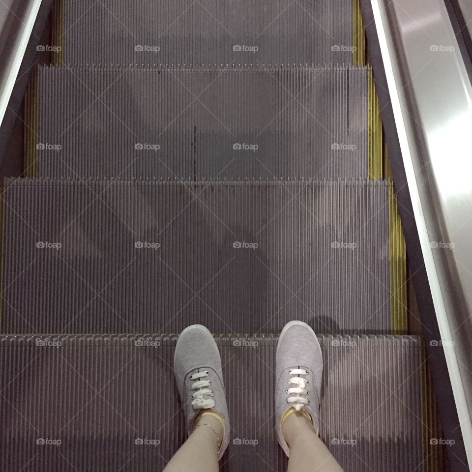 Woman standing at escalator. Woman Standing at Escalator, Sneakers at Staircase from Above, Top View