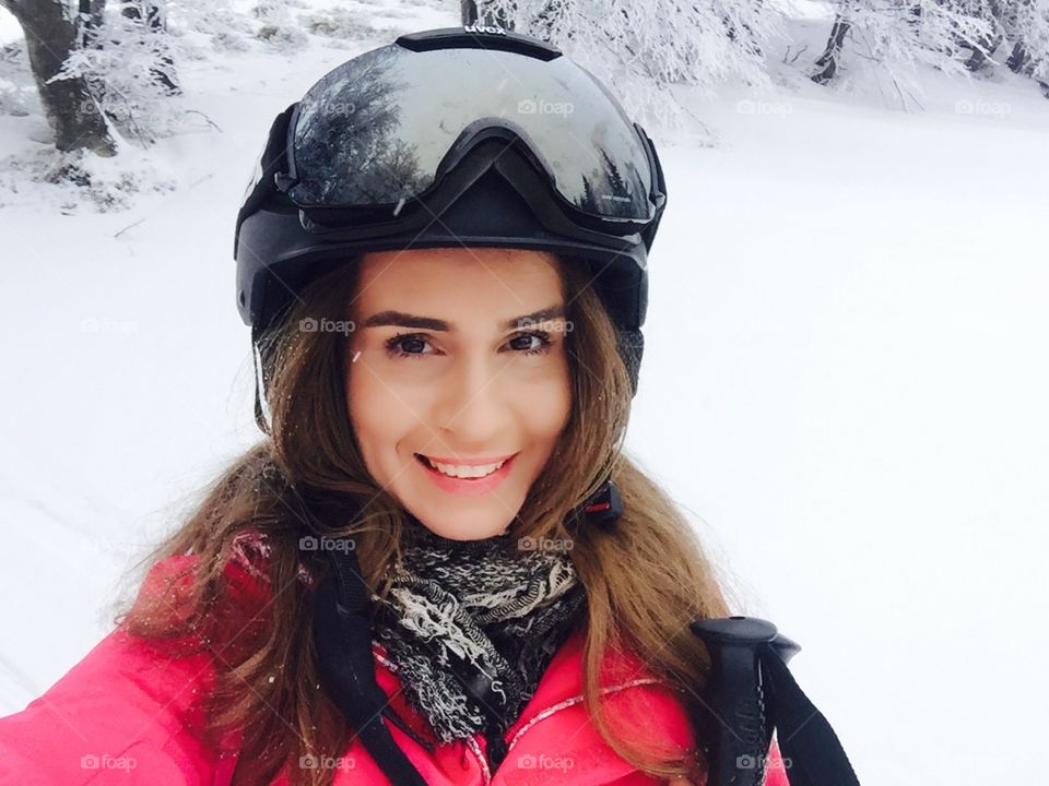 Selfie of pretty woman wearing uvex ski glasses and uvex ski with trees covered in snow in the background