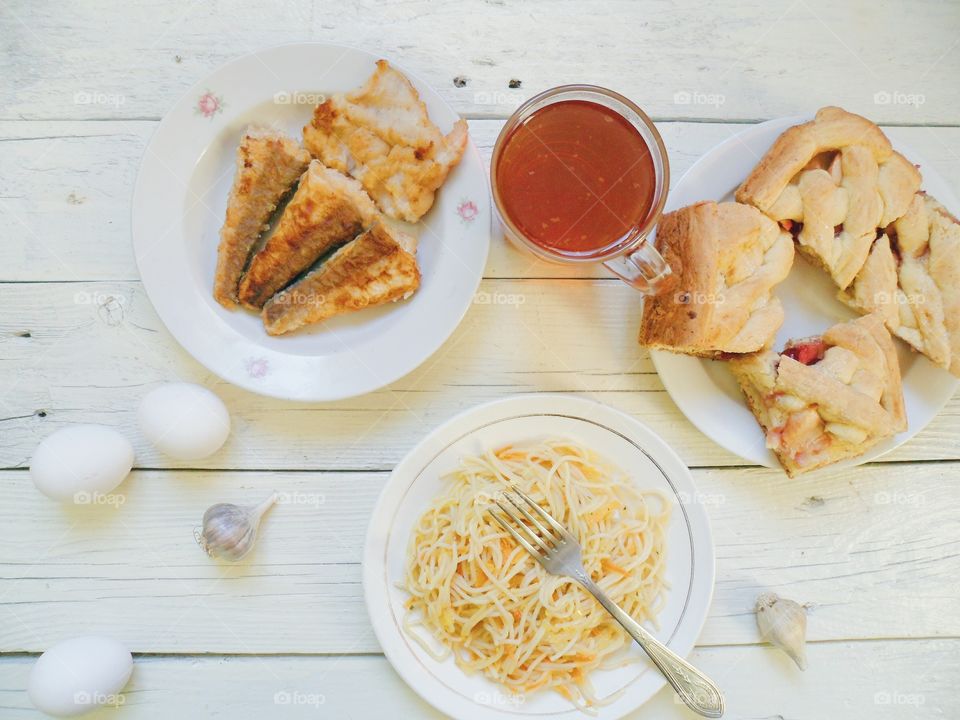 noodles in a dish, homemade cake, fried fish and a cup of tea on the table