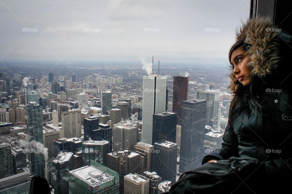 Teen girl on a window sill is looking at the city