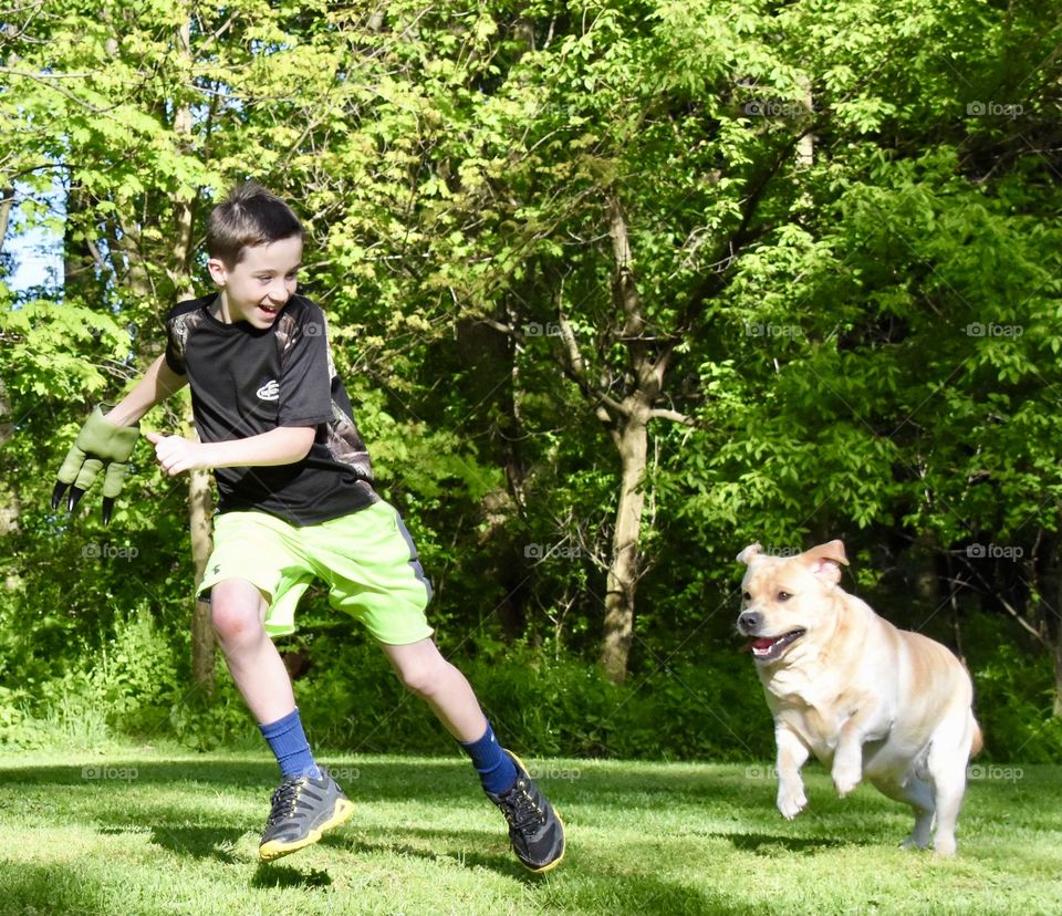 A boy and his dog running and playing on a sunny afternoon in the back yard