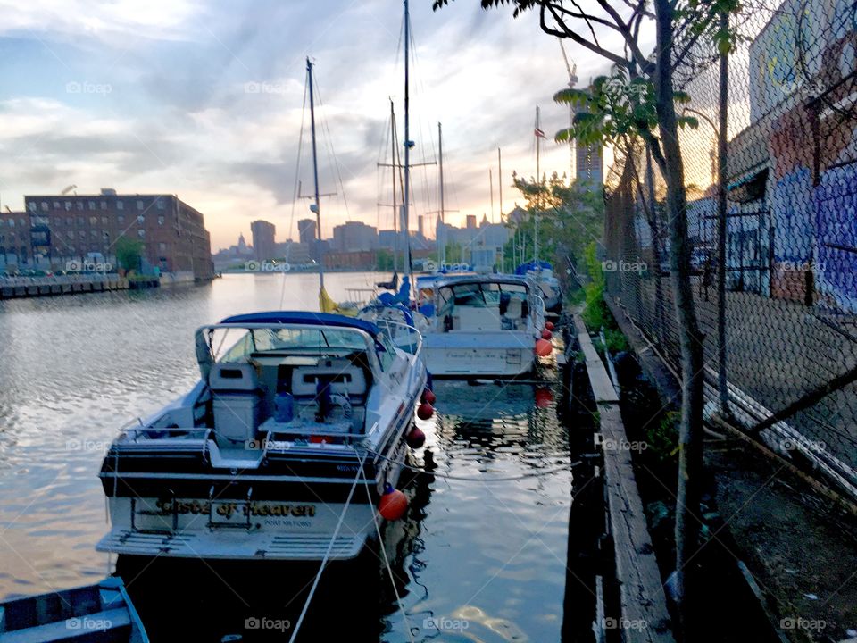 Sailboats in the East River at Newtown Creek, LIC, Queens, NY. The sun has set and only a hint of magenta pink is still reflecting in the clouds. At the horizon you can see the Manhattan skyline as well as parts of Queens. 2018 Hypnotic Productions