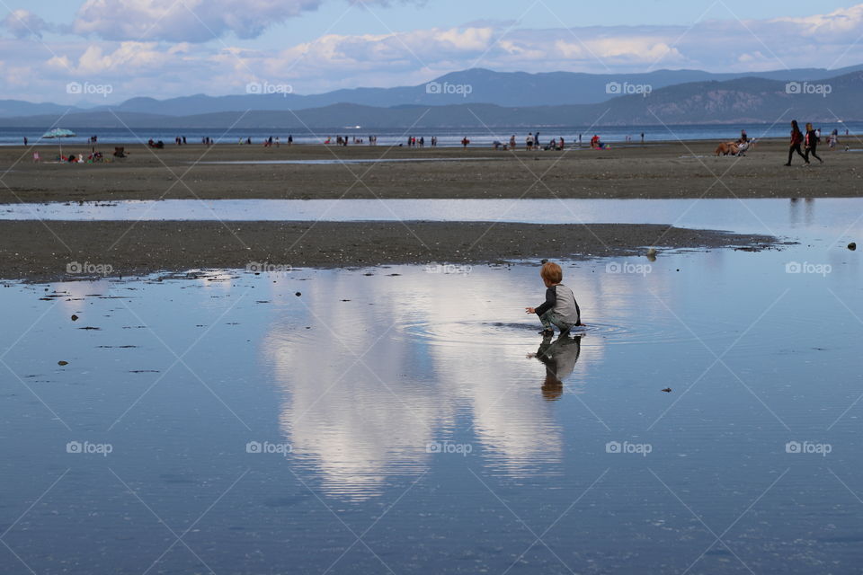 Kid sitting in a puddle of waterwheel clouds  reflect during low tide 