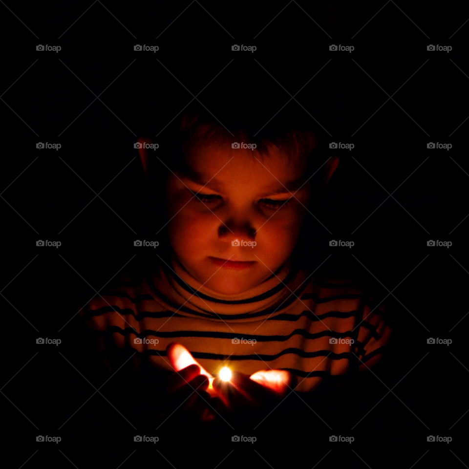 A child in the dark with a burning candle in his palms