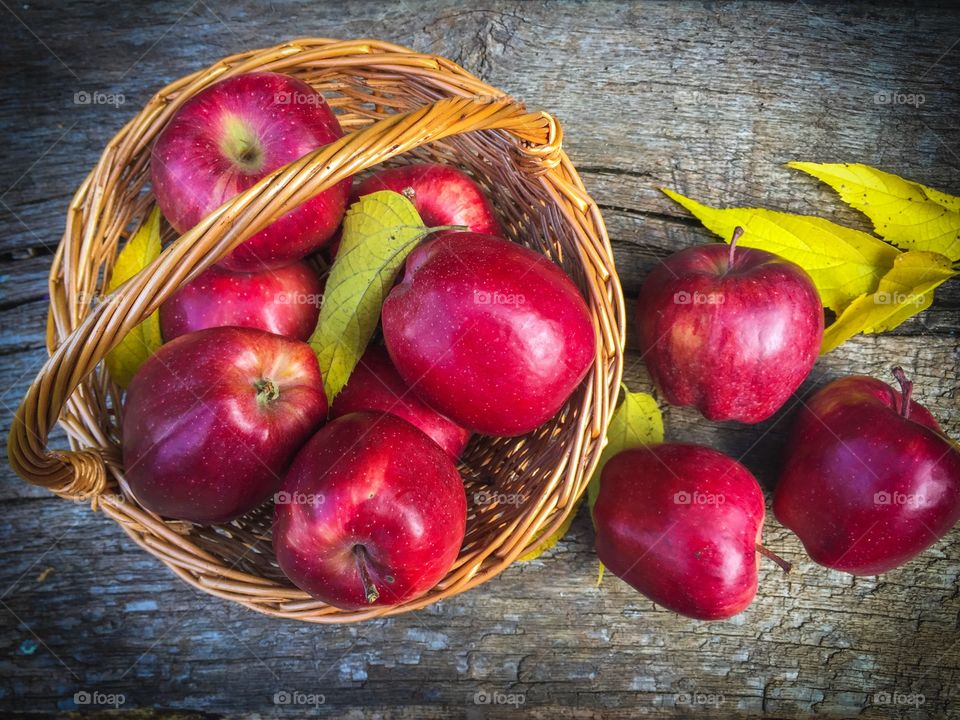 Wooden basket full of red appples and yellow leaves