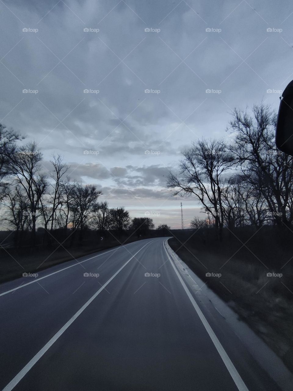 On the highway. Car road trip. Wet gray asphalt highway, trees along the road.  Beautiful sunset clouds. Driving on the highway. Eastern Europe, Ukraine