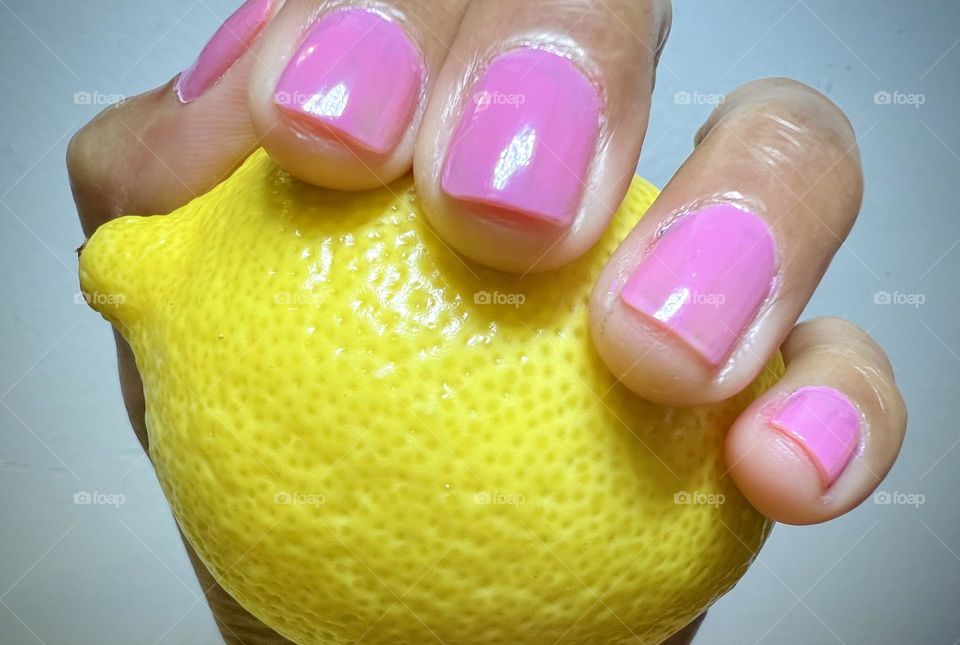 A person holding a lemon with pink nail polish.