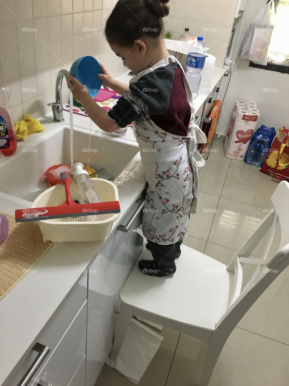 A girl uses a chair to help parents wash dishes