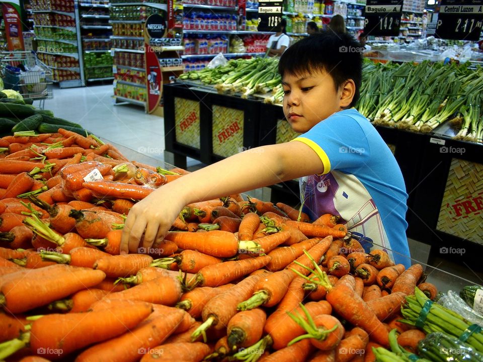 young boy getting vegetable from a shelf in a grocery store