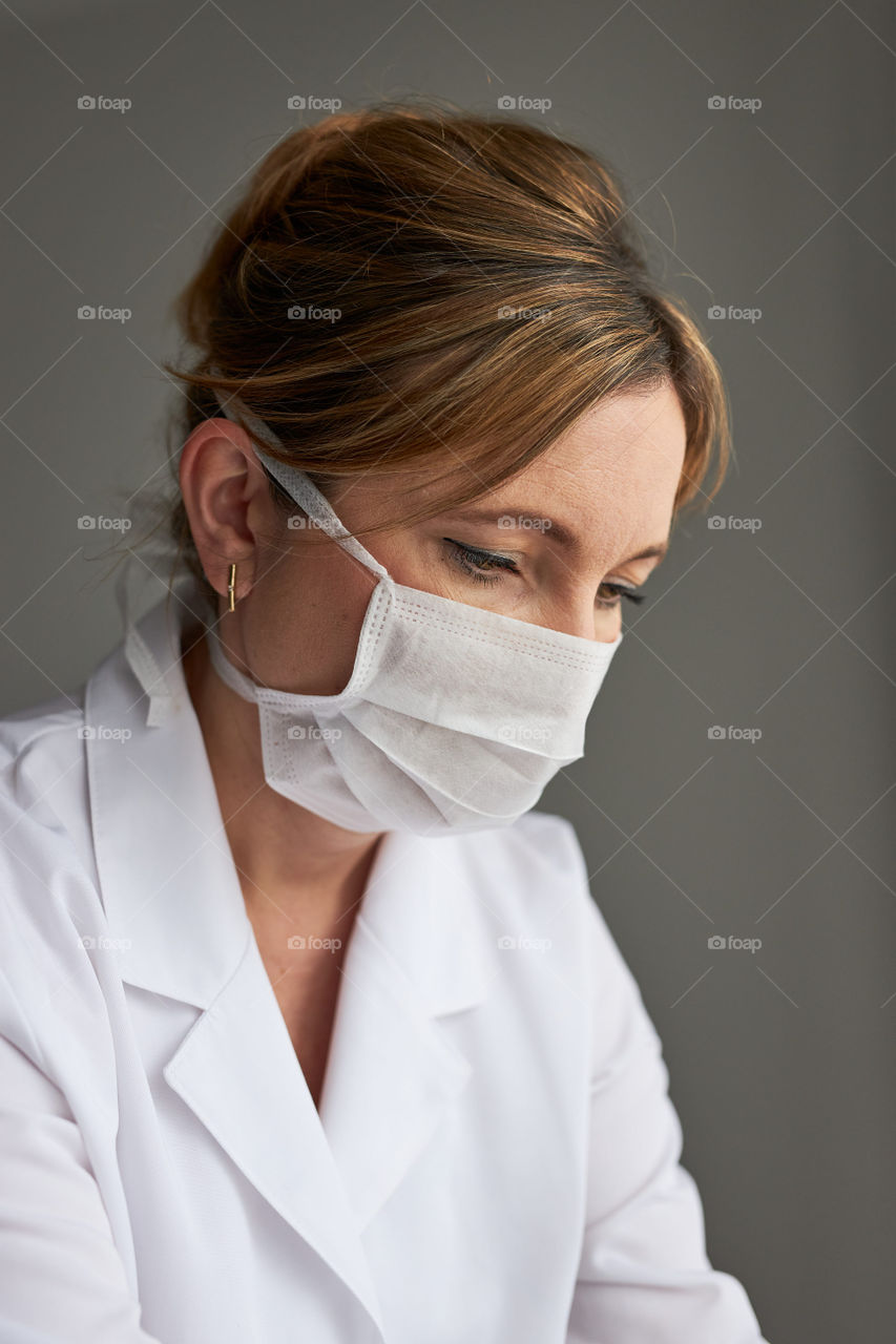 Doctor with face covered with mask. Portrait of young woman wearing the uniform, cap and mask to avoid virus infection and to prevent the spread of disease. Real people, authentic situations