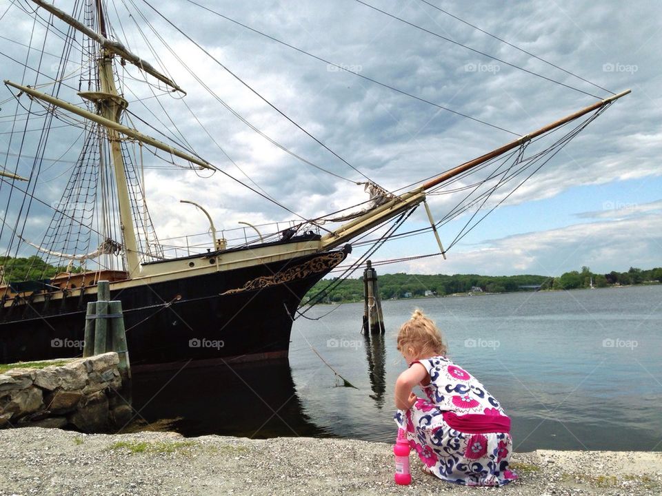 Little girl plays by the water and vintage schooner 